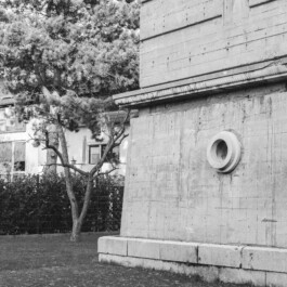 Betonwand eines Bunkers mit runder Lüftungsöffnung neben Wohnhaus 