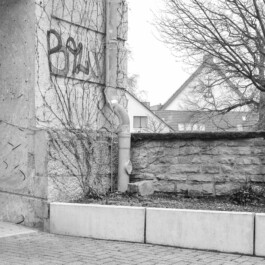 Graffiti und Rohrleitung an Bunkerwand neben niedriger Mauer 